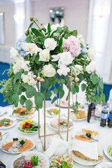 Bouquet of white roses and blue hydrangeas stands in the middle of dinner table
