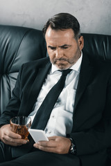 businessman with glass of whiskey using smartphone