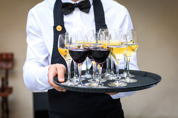 Professional waiter in black uniform serving red and white wine.