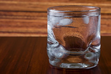 Glass of vodka and ice on wooden background