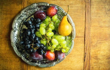 Fresh fruit assortment on silver tray on wooden background. Ripe grapes, plums and pear, top view