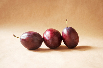 Three purple plums on paper background, still life