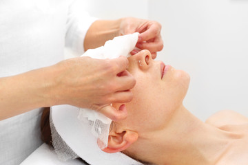 Pielęgnacja skóry w klinice medycyny estetycznej. Kosmetyczka zdejmuje pacjentce bandaż z twarzy.