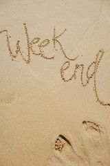Weekend inscription on the sand of a clean beach along with footprints of women.