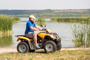 Obraz premium Caucasian man riding an ATV quad bike over rough terrain near lake or river shore with bulrush and reed. Adventure activity concept