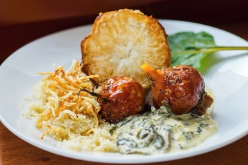 Baked roots and celery, couscous and spinach on white plate.