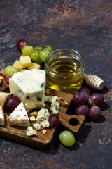 cheeseboard, fruits and honey on a dark background, vertical, top view