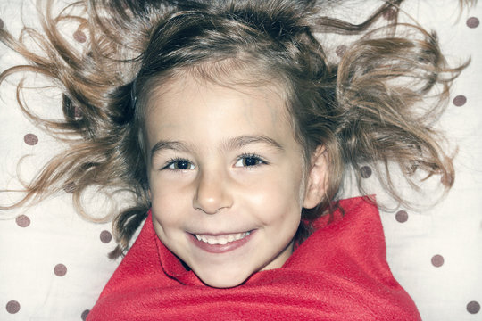 A Truly Beautiful Little Girl With Shaggy Hair On The Pillow In Red Plaid