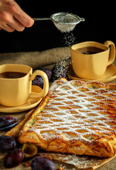 The girl sprinkles with sugar powder an apple strudel made of puff pastry