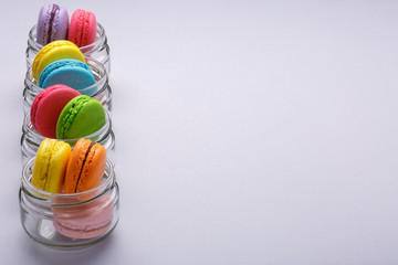Colorful tasty macaroons in glass jars on gray background