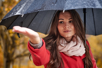 A girl in a red coat with a black umbrella in the rain in the autumn