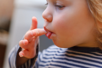 funny baby toddler blonde boy licks a finger - obrazy, fototapety, plakaty