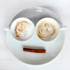 double invigorating cappuccino/ Two white cups with frothy coffee and cinnamon stick on a plate top view