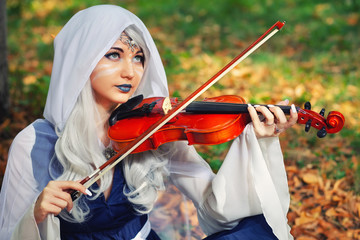 Elf with a violin in the autumn forest. Beautiful Girl In an elf costume playing a musical...