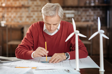 Grey-haired man using protractor while drawing blueprint