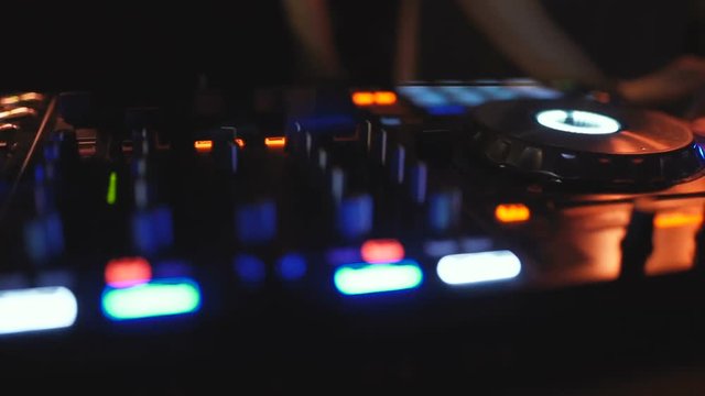 Hands of woman DJ tweak various track controls on dj's deck at night club 
