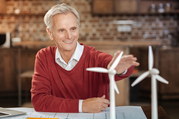 Joyful senior man reaching a hand towards wind turbine models