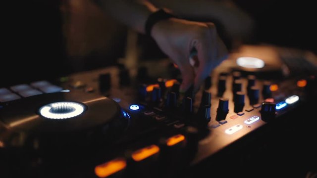 Hands of woman DJ tweak various track controls on dj's deck at night club 