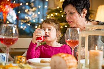 Happy family celebrating holiday together, sitting around decorated round table, Grandma and kid . Living room with Christmas tree, lights and candles. Merry Christmas concept