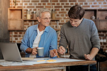 Pleasant mentor helping young colleague draw blueprint