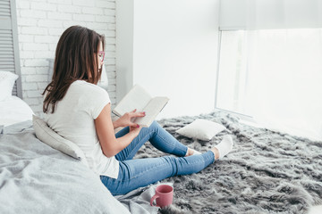 Beautiful young woman sitting on the floor and reading a book, back view