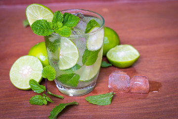 Fresh Mojito cocktail with fresh green limes, mint and ice on wooden background.