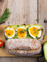 Avocado and egg sandwich on a wooden background. Fresh organic vegetables, eggs and whole wheat bread. Healthy breakfast. Rustic style.