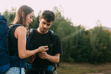 Young couple with backpacks looking at compass 