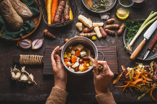 Female Woman Hands Holding Pan With Diced Colorful Vegetables And A Spoon On Rustic Kitchen Table With Vegetarian Cooking Ingredients And Tools. Healthy And Clean Food  Cooking And Eating  Concept.