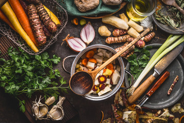 Pot with sliced colorful vegetables and cooking spoon on dark rustic table background with organic vegetarian ingredients and kitchen tools , top view. Healthy and clean food and eating  concept.