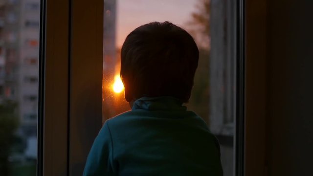 a child stands on the windowsill and looking out the window at the sun. Sunset
