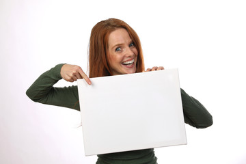 Hübsche rothaarige Frau mit weisser Tafel in der Hand lacht und zeigt auf die Tafel