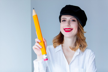 Young redhead woman in hat holding chuge pencil