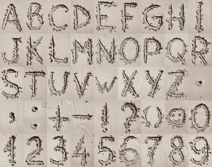 Handwritten English alphabet, numbers and mathematical symbols on the sand.