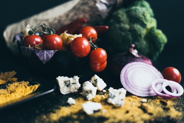 A bottle of red wine, delicious fresh tomatoes cherry and red hot chili peppers in a black dish lying on a wooden cutting board. Herbs, blue cheese, a red onion and broccoli are used as a decoration.