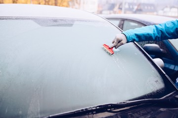 Woman removing ice from car windshield with glass scraper.