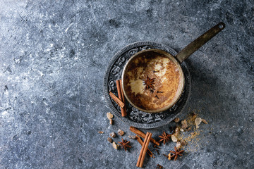 Vintage pot of traditional indian masala chai tea with ingredients above. Cinnamon, cardamom,...