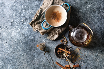 Vintage blue pot of traditional indian masala chai tea with ingredients above. Cinnamon, cardamom,...