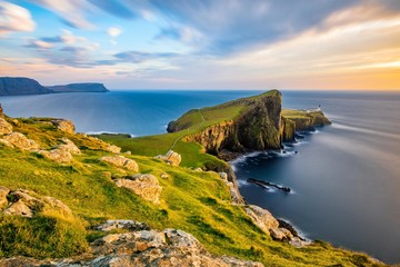 Neist Point Lighthouse on the Isle of Skye bathed in golden light from the setting sun. - obrazy, fototapety, plakaty