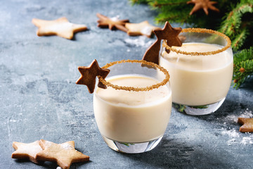 Eggnog Christmas milk cocktail with cinnamon, served in two glasses with shortbread star shape sugar cookies different size, decor toys, fir branch over blue texture background. © Natasha Breen