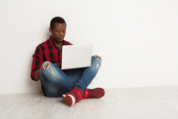Thinking black man using laptop sitting on the studio floor