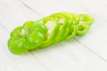 Sliced green fresh raw pepper on old rural white wooden planks