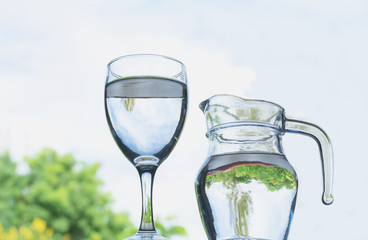 Water glass with water pitcher under the sky on table.