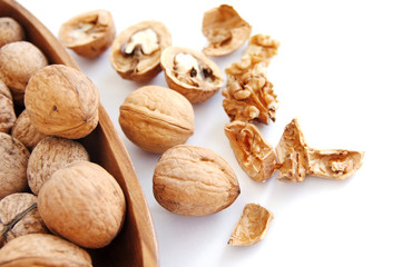 Walnut kernels in a wooden bowl and whole walnuts on a white background. Walnuts