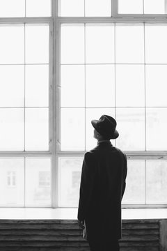 Man dressed in coat and hat standing in front of window
