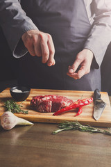 Chef seasoning rib eye steak on wooden board at restaurant kitch