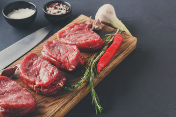 Filet mignon steaks and spices on wood at black background