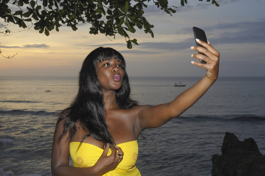 glamorous African American black woman in chic summer dress taking selfie picture or video on mobile phone