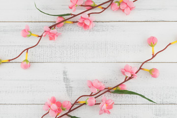 Fake pink flower branches on white wood background with copy space