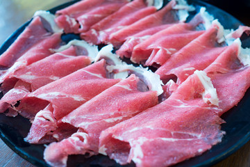 Slide raw pork meet on black plate for shabu and sukiyaki.